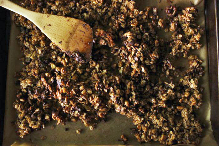 Vegan Chocolate Cinnamon Granola on a baking tray with a wooden spoon.