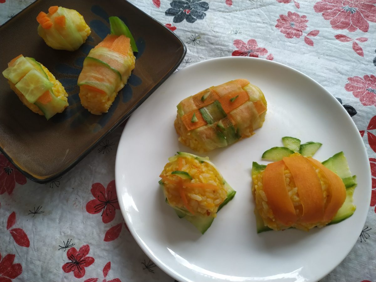 A plate of halloween themed sushi with pumpkin, carrot, rice, and cucumber