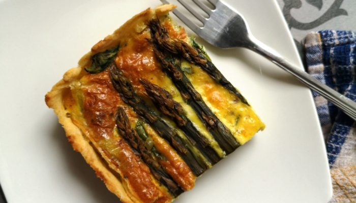 vegan spinach asparagus pie on a white plate with a fork