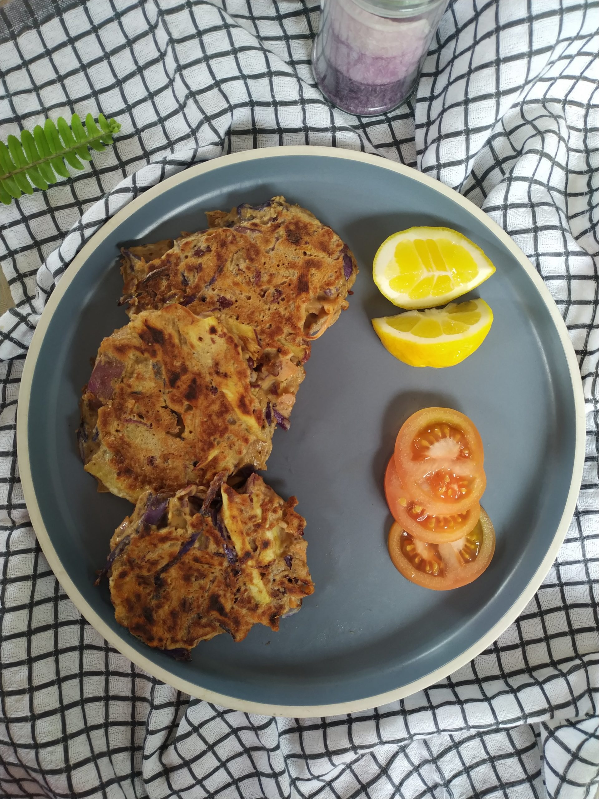 vegetable fritters on a blue plate with slices of tomato and lemon next to a candle and a fern