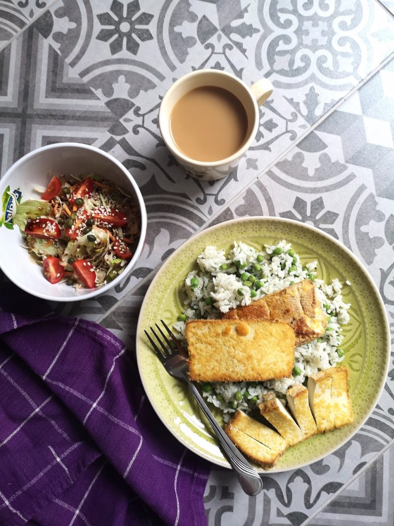 tofu schnitzel with rice and peas on a green plate with a fork