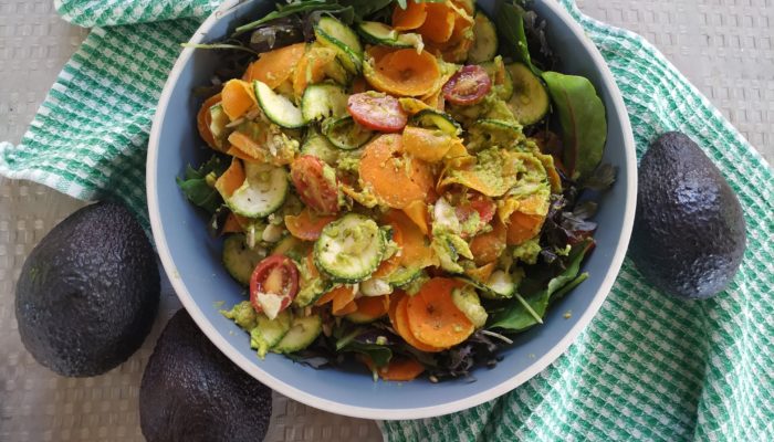 vegan south east asian rainbow salad with creamy peanut avocado sriracha dressing in a bowl next to avocados