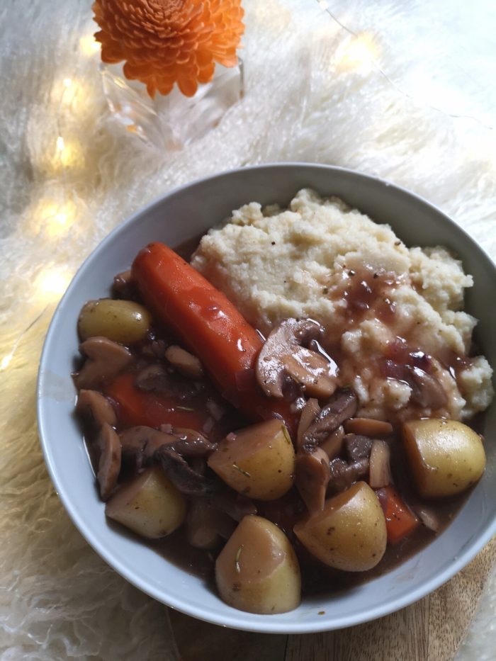 vegan coq au vin against a white background with lights and a flower