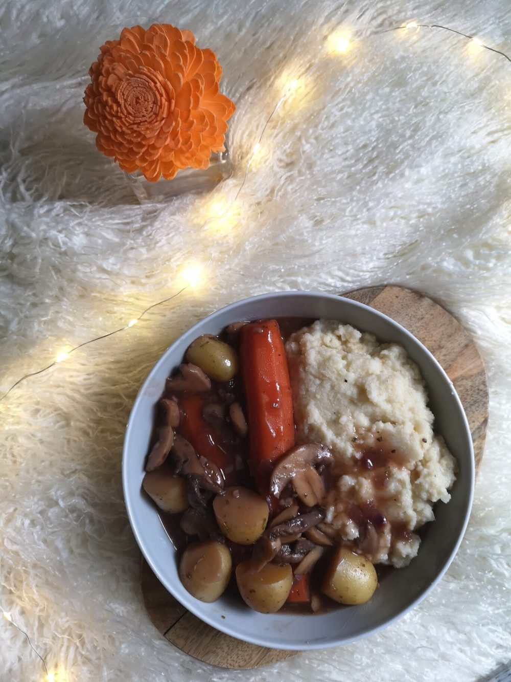 vegan coq au vin against a white background with lights and a flower