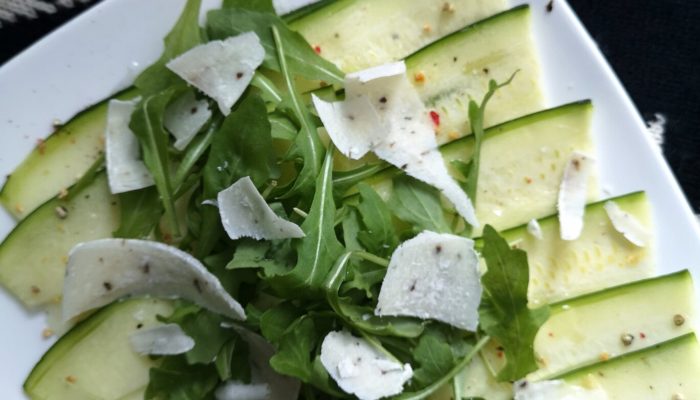 zucchini carpaccio salad with vegan truffle cheese on a white plate