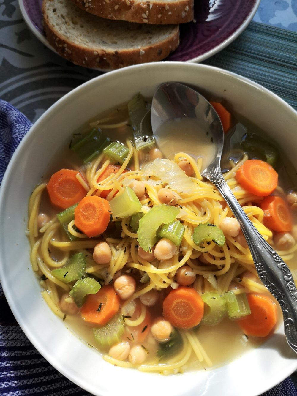 vegan chickpea spaghetti soup in a bowl with a spoon next to bread slices on a plate