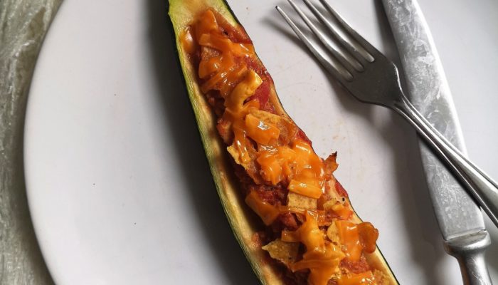 vegan nacho stuffed zucchini boat on a white plate with a fork and knife