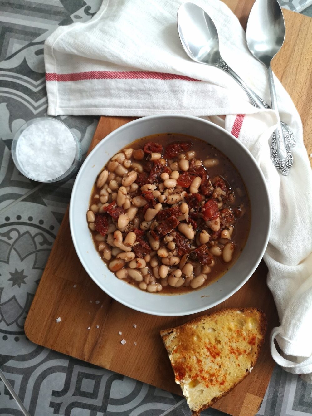 beans soup in a white dish on a table next to bread slices