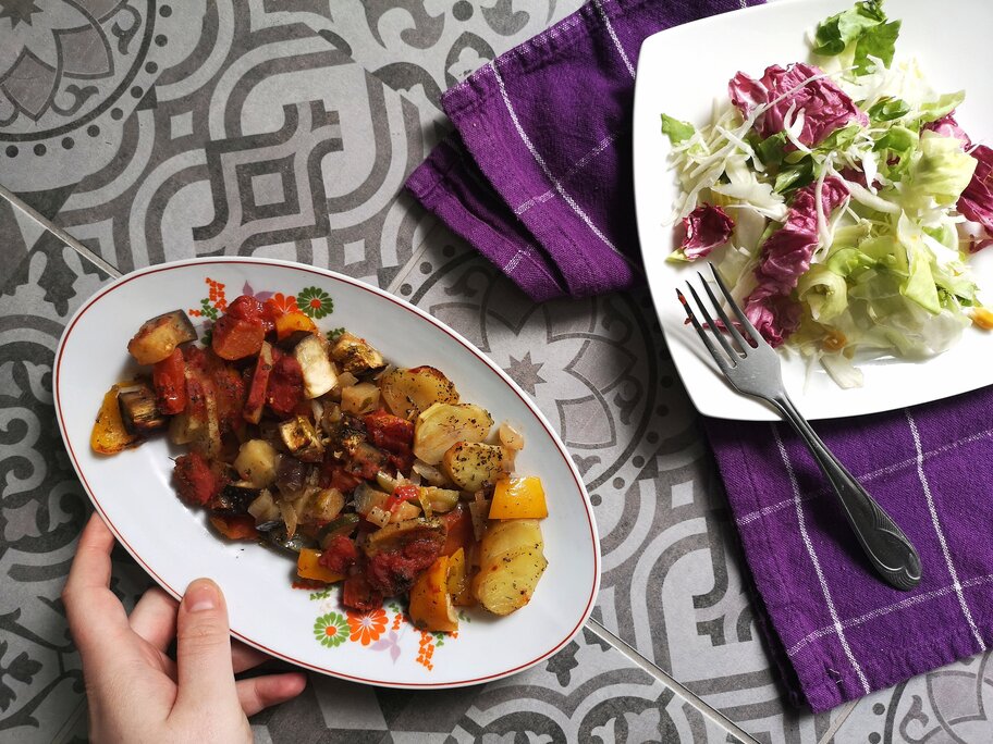 vegan briam (vegetable bake) on a white dish with a fork next to a plate of salad