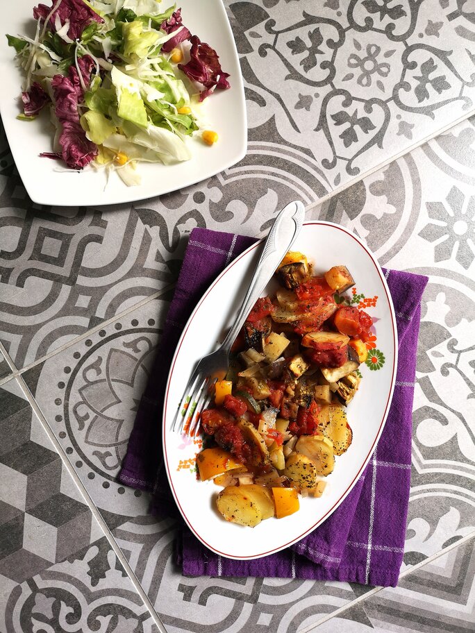 vegan briam (vegetable bake) on a white dish with a fork