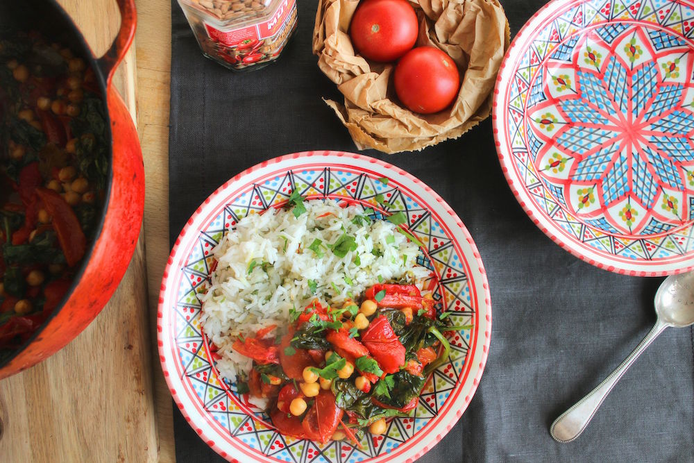 chickpea stew on a decorative plate next to tomatoes and silverware