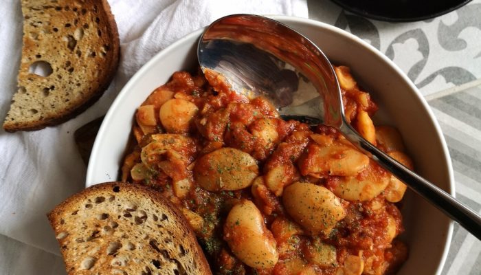 gigantes beans in a white bowl with bread and a silver spoon