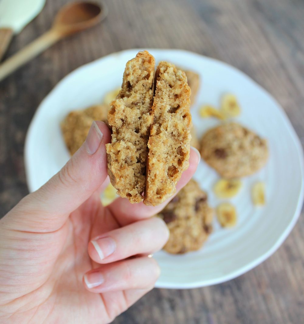 a hand holding a banana chocolate chip oatmeal cookie above cookies on a white plate