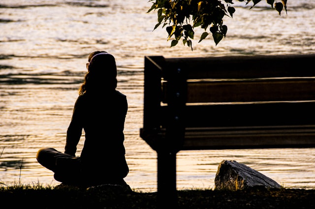 Silhouette meditating by the water