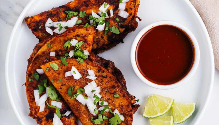 vegan quesabirria tacos on a white plate with dipping sauce and limes