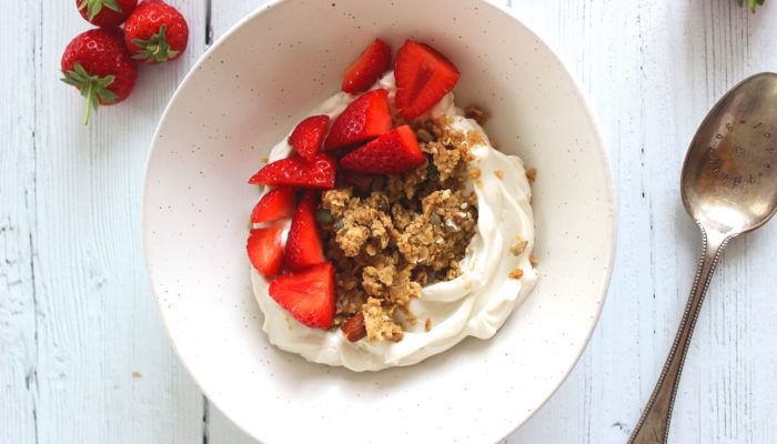 peanut butter granola in a bowl with strawberries against a white background