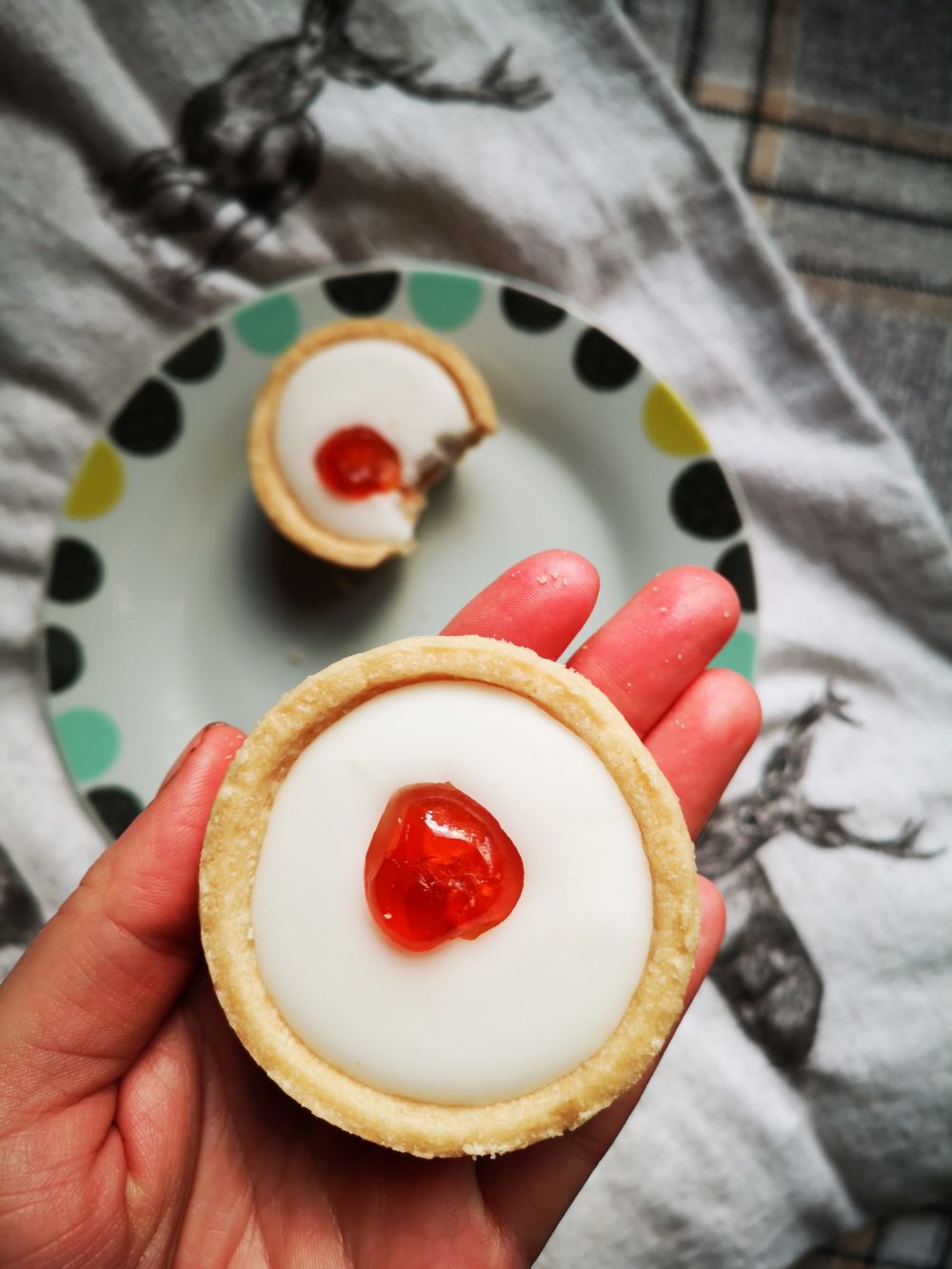 a hand holding a mini cherry tart above a decorative plate