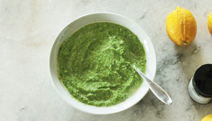 broccoli soup in a white bowl on a table with lemons