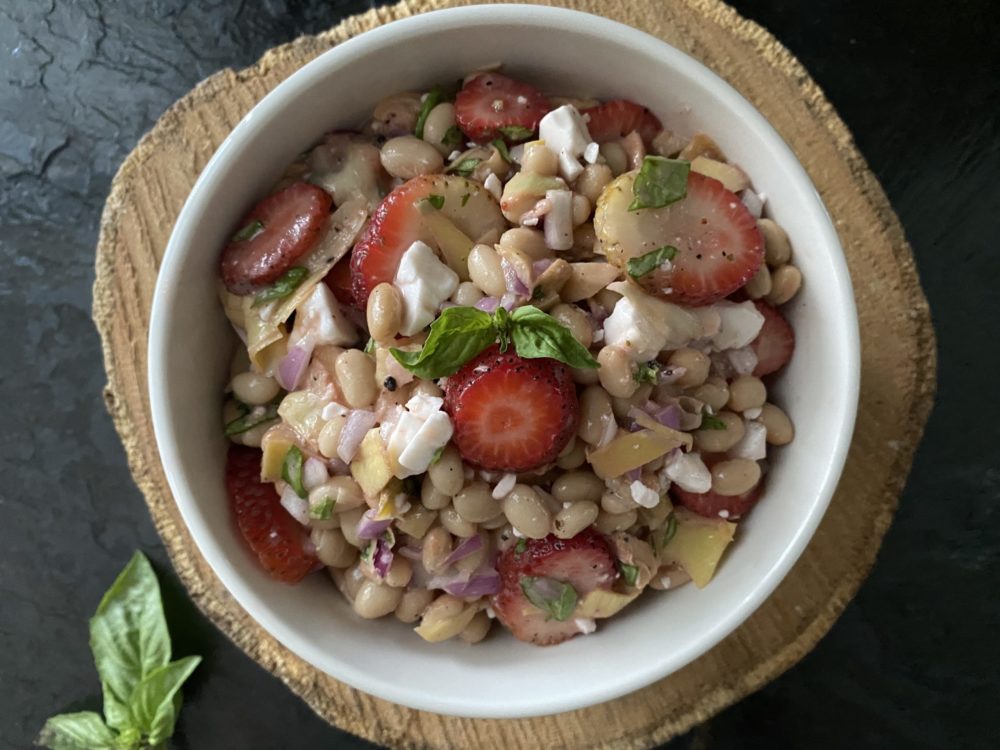 white bean artichoke salad in a white bowl against a brown and black background