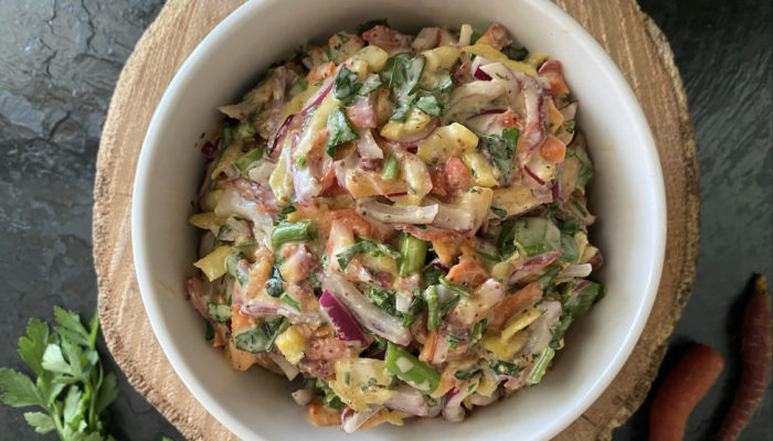 carrot salad with lemon dijon dressing in a white bowl agaisnt a brown and black background