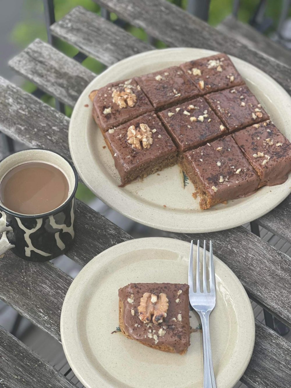 vegan coffee walnut cake with chocolate custard frosting on white plates next to a mug on a wooden table