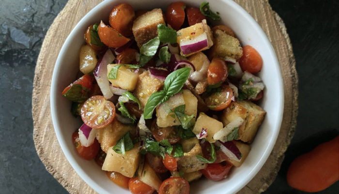 cantaloupe panzanella in a white bowl against a brown and black background