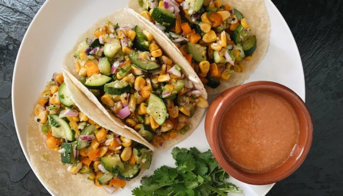 zucchini corn tacos on a white plate against a dark background