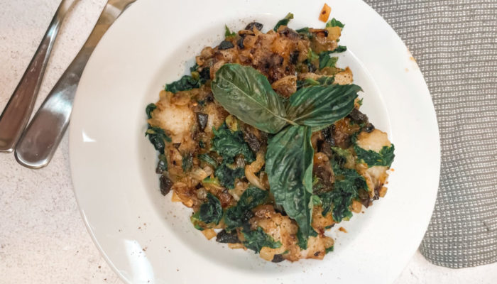 black garlic gnocchi on a white plate next to a gray towel and silverware