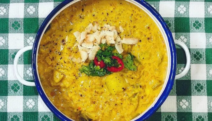 spicy vegetable curry in a white and blue bowl against a green/white table top