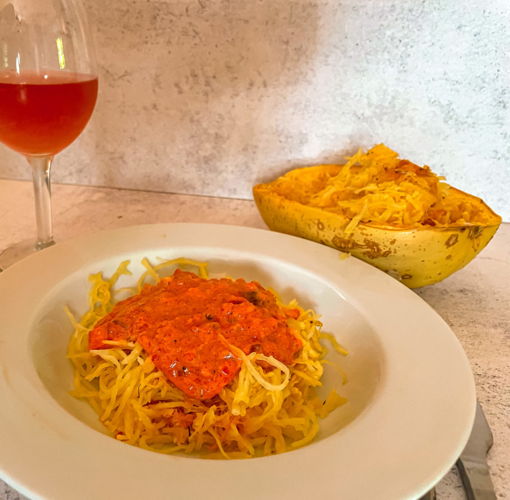 roasted red pepper squash noodles in a white dish in front of a drink and spaghetti squash