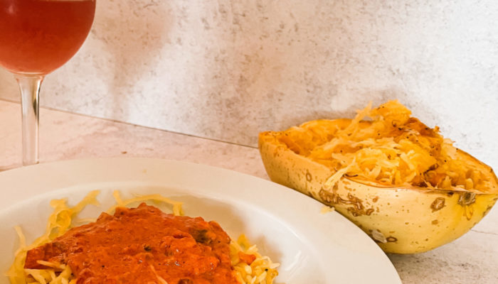 roasted red pepper squash noodles in a white dish in front of a drink and spaghetti squash