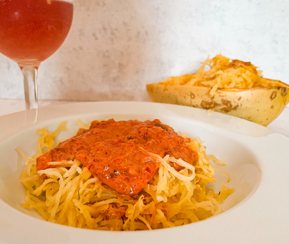 roasted red pepper squash noodles in a white dish with a glass and squash in the background