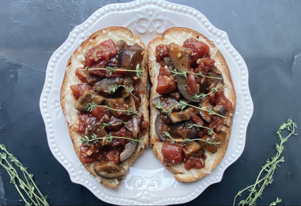 vegan eggplant bruschetta on a white plate against a dark background