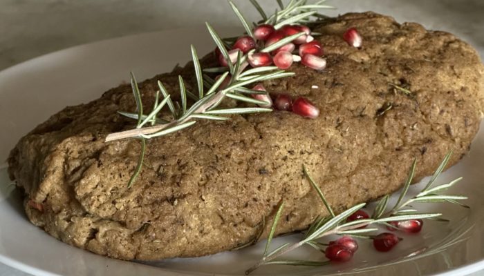 Vegan turkey on a white plate with pomegranate seeds and greens