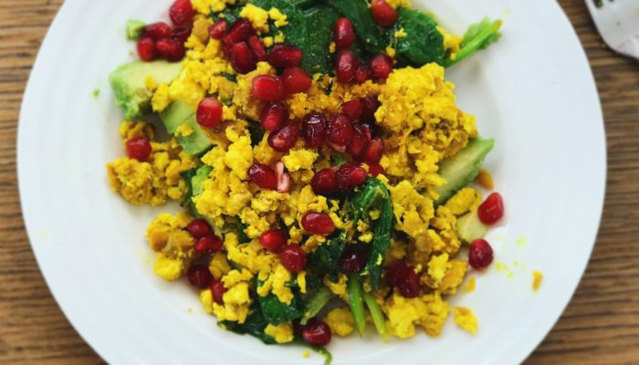 tofu scramble with pomegranate seeds on a white plate on a wooden table