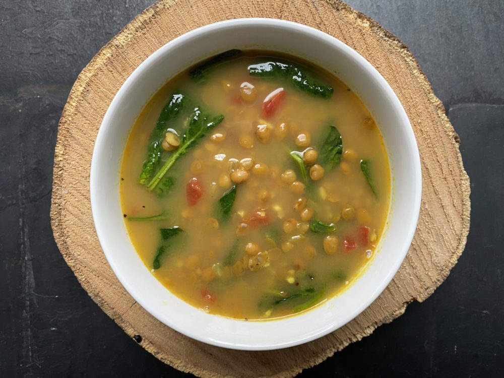 yellow-colored lentil dal soup in a white bowl against a black background.