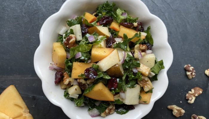 persimmon kale salad in a white bowl against a dark background