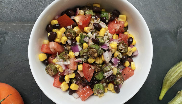 vegan okra tomato salad in a white bowl against a dark background