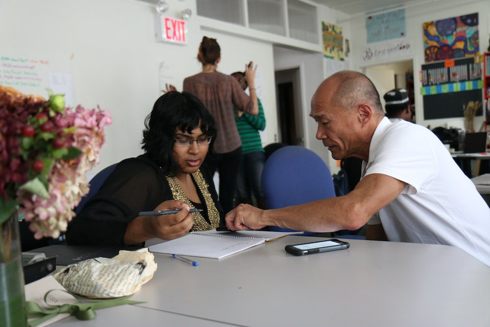 a Black woman activist and a middle-aged Asian man at a table discussing issues. 