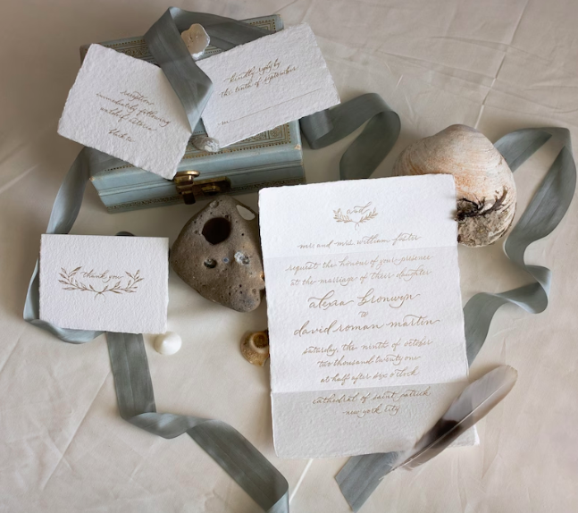 handmade paper wedding invitation suite with deckled edges and letterpress printing in gold, surrounded by blue ribbons. 