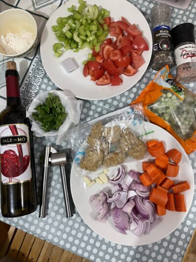 chopped tomatoes, celery, onions, carrots, a bottle of red wine, and seasoning laid out on a table.