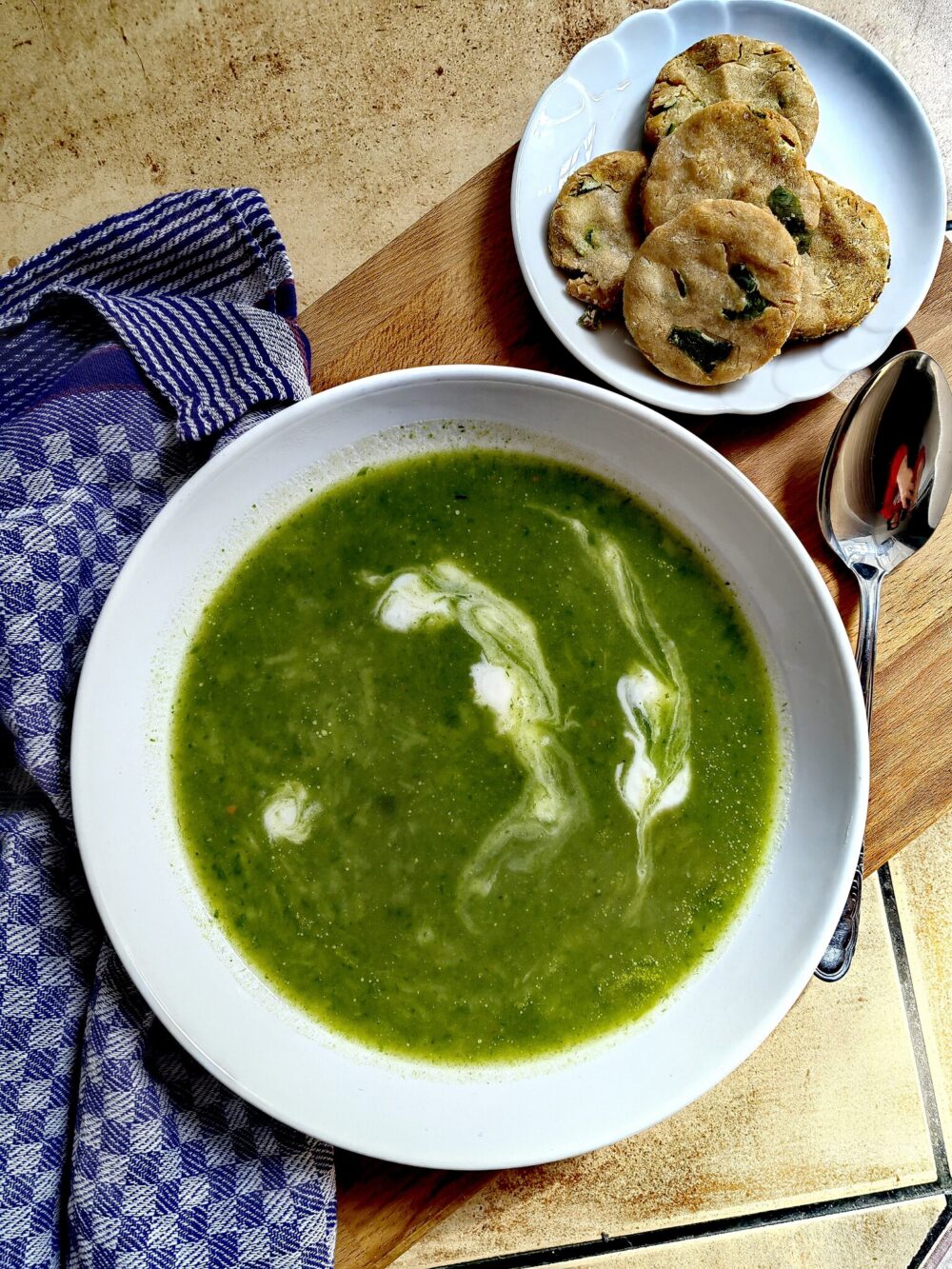 creamy green wild garlic soup in a white bowl on a wooden table with some crackers on the side.