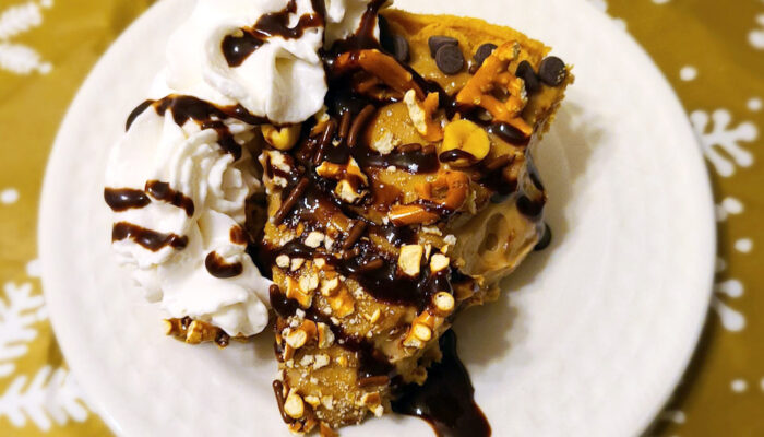 a slice of vegan chocolate peanut butter pretzel pie on a white plate against a tablecloth with snowflakes