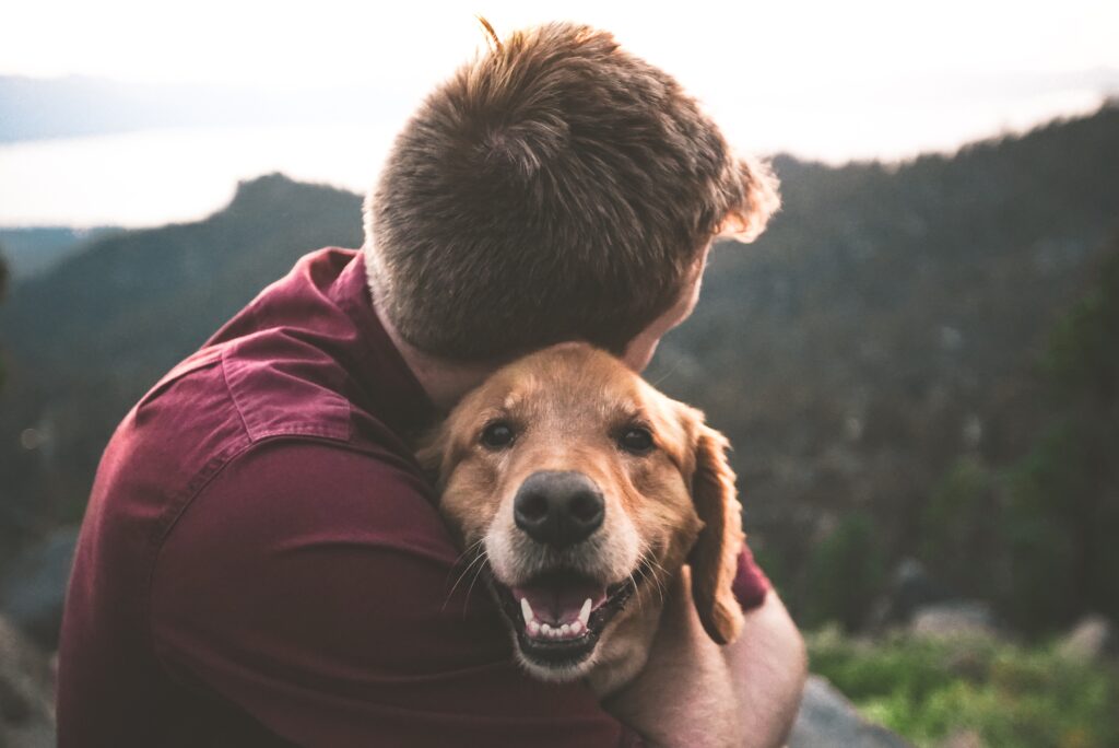 a man hugs a golden retriever with mountains in the background.