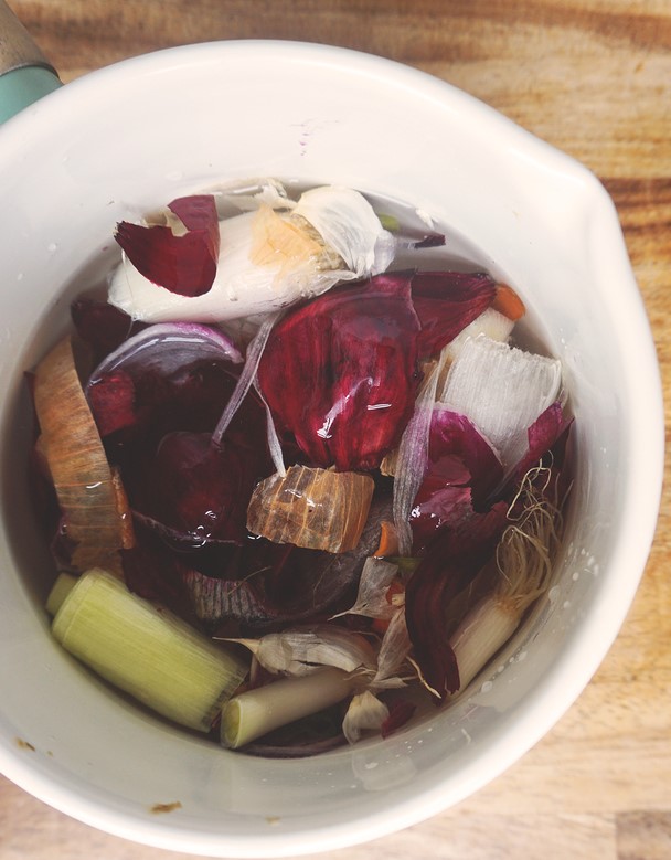 vegan broth with kitchen scraps in a white bowl on a wooden countertop.