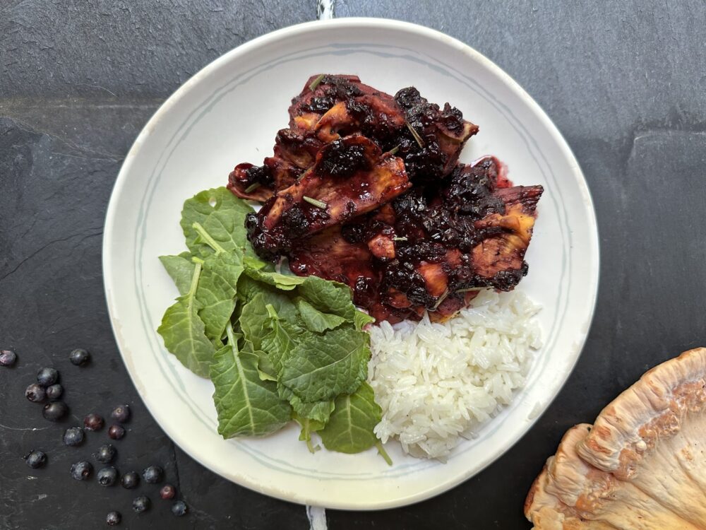 chicken of the woods dish glazed with blueberry balsamic sauce, garnished with herbs and white rice on a white plate on a black countertop.