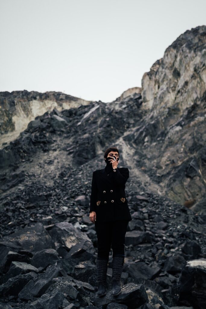 a woman wearing black standing in a coal mine, covering her nose and mouth.