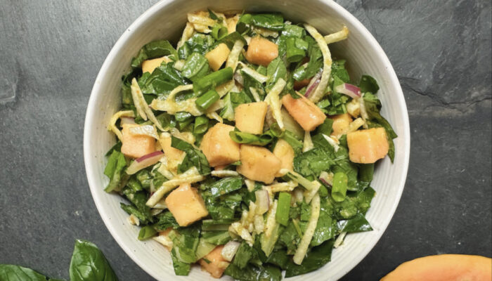 green-based papaya salad in a white bowl on a black granite countertop