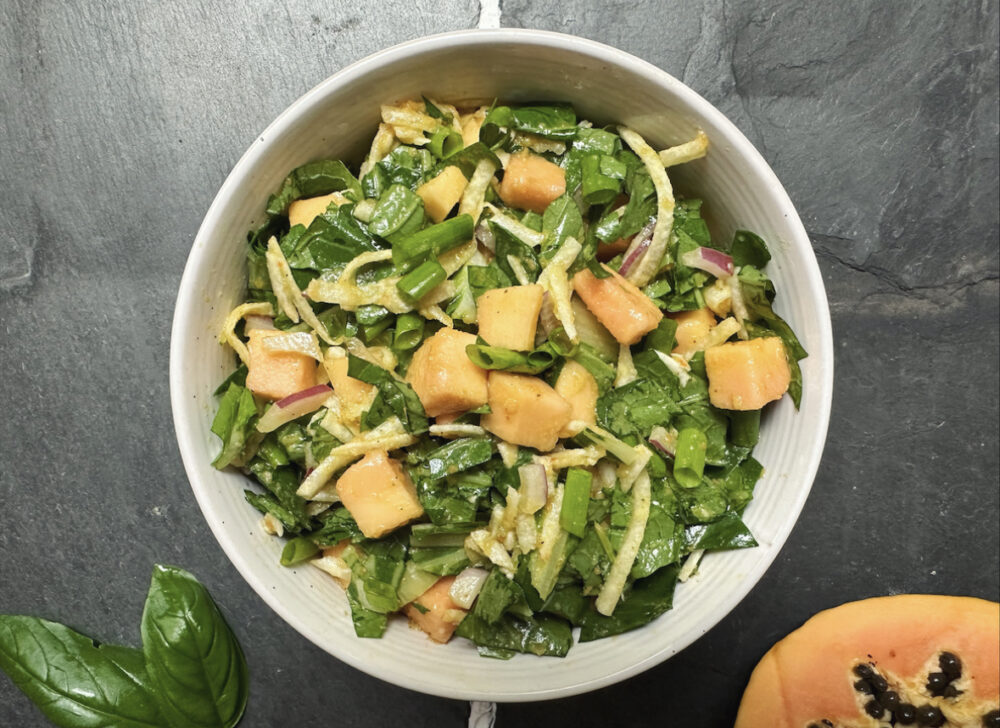 green-based papaya salad in a white bowl on a black granite countertop